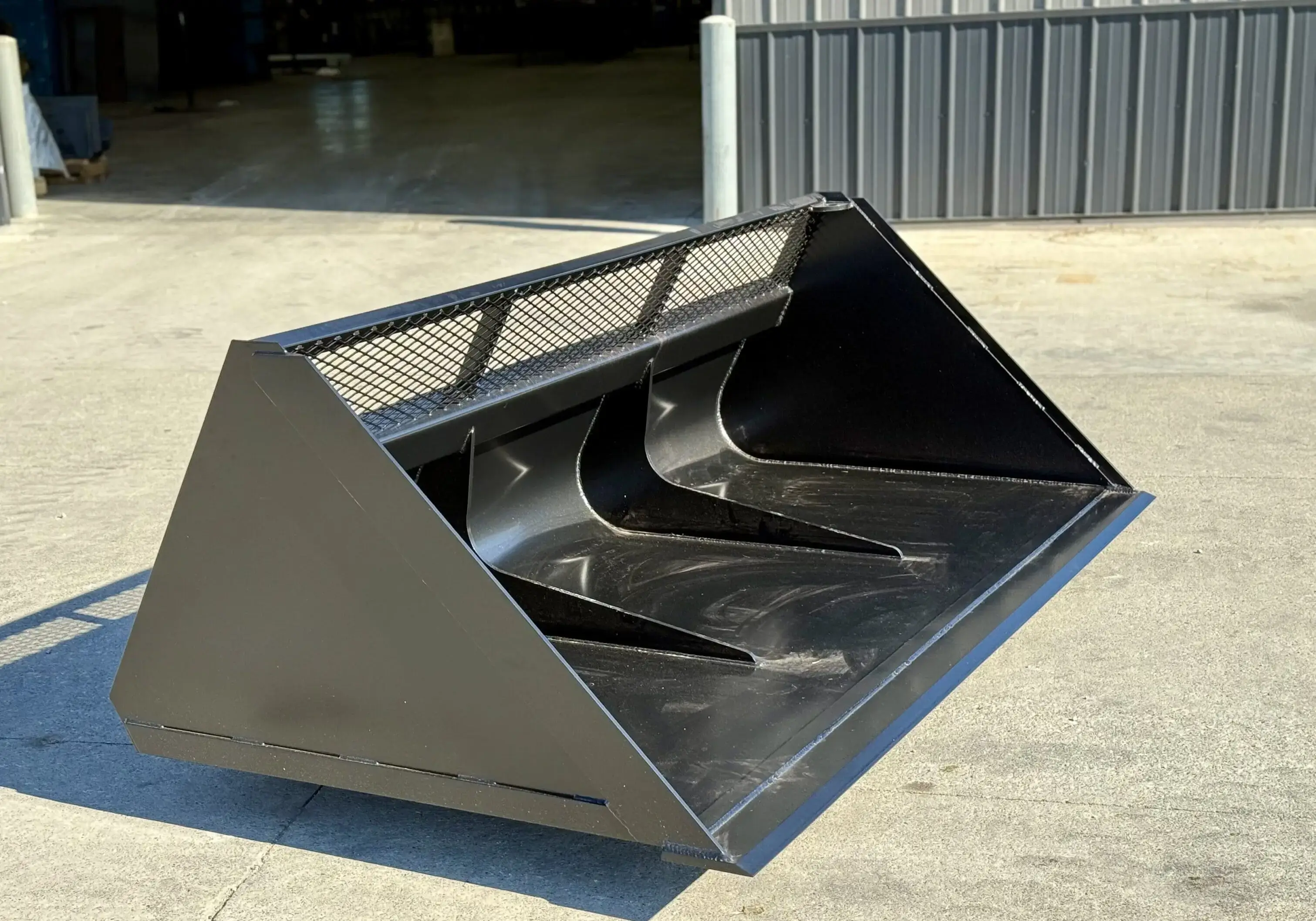 Large black metal bucket attachment for heavy machinery on concrete.